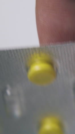 man holds silver blister with little bright yellow pills above light background extreme close view