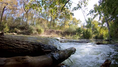 Panning-left-past-two-logs-just-out-of-the-water,-sitting-where-the-waterfall-begins-its-drop