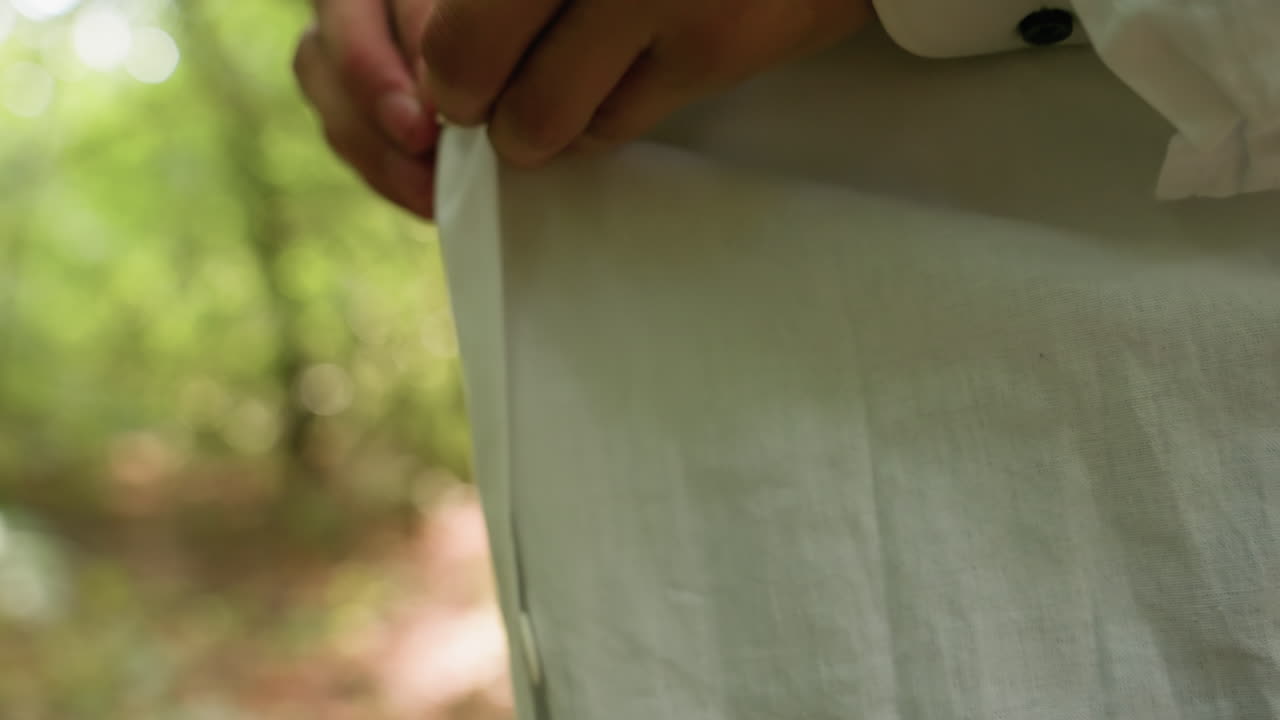 Close up view of botany student in white shirt buttoning coat in blurred forest, highlighting natural greenery, outdoor lifestyle, preparation, concentration, and detail of scientific readiness