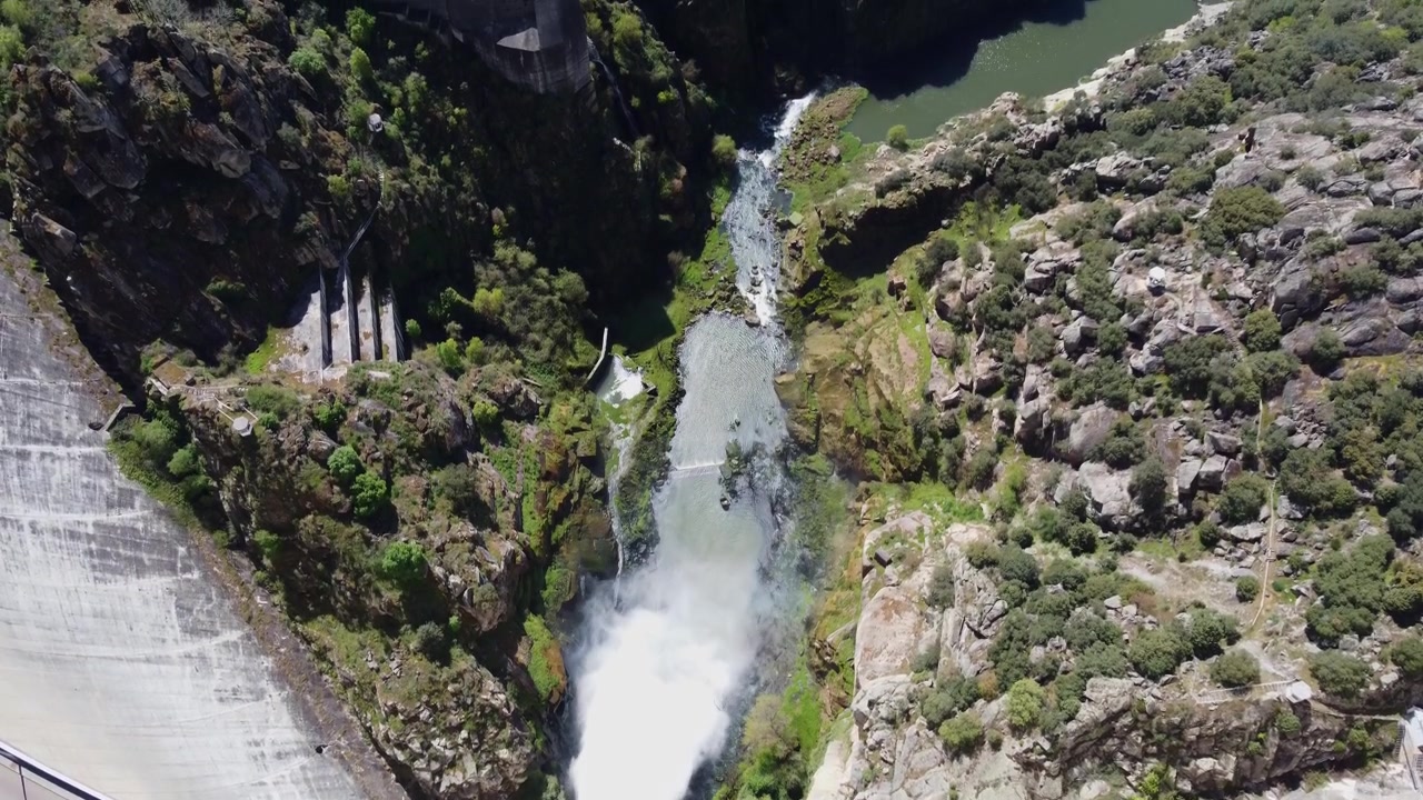 Ripresa aerea 4K con drone con una lenta rotazione della telecamera sopra l'imponente diga in cemento di Almendra in Spagna. La vista rivela un potente rilascio d'acqua che forma un fiume attraverso la gola rocciosa di montagna in una giornata di sole.