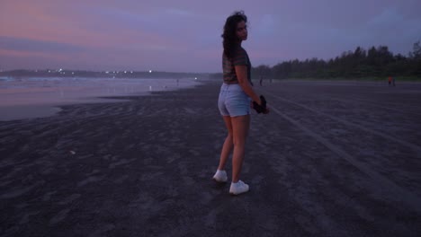 landscape view of a young woman walking on a sandy beach, and looking back, by the ocean, during a purple sunset