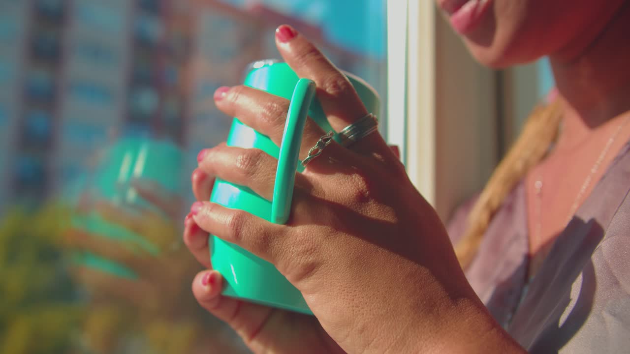 primer plano de una taza de café o té en la mano de una chica de raza mixta con uñas rojas en la soleada mañana de verano, fotograma completo