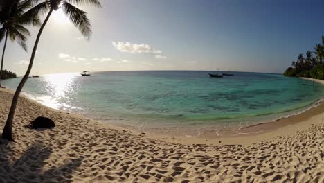 la luz del sol que se refleja en el agua turquesa lavando suavemente una playa de arena prístina con palmeras y barcos en la distancia crea un sereno paraíso tropical