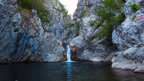 Waterfall-Boaza-Waterfall-with-Stony-Cliffs-Overgrown-with-Trees-to-the-Right-with-a-Small-Lake-in-Slow-Motion-4K