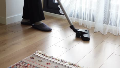 person vacuuming a wooden floor with rug