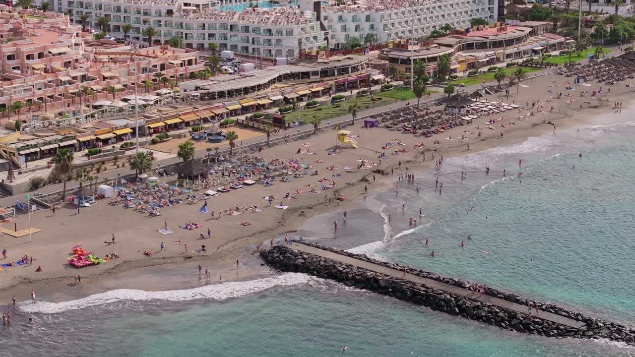 Lively Costa Adeje beach resort with sunbathers, waves, and oceanfront hotels