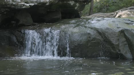 imágenes de cerca de una pequeña cascada saliendo de una roca en un arroyo