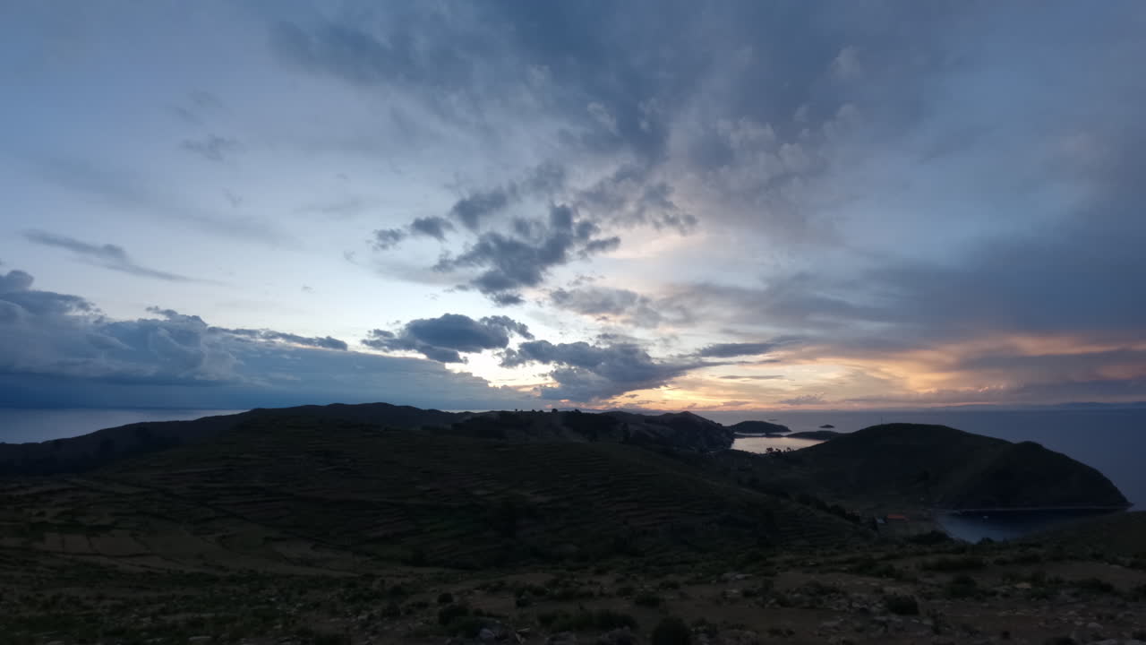 남미 볼리비아의 일몰의 타임 스: 구름이 카메라를 향해 빠르게 움직이고 하늘이 파란색, 분홍색, 보라색으로 변하며 섬 주변에서 물과 바다가 보인다.