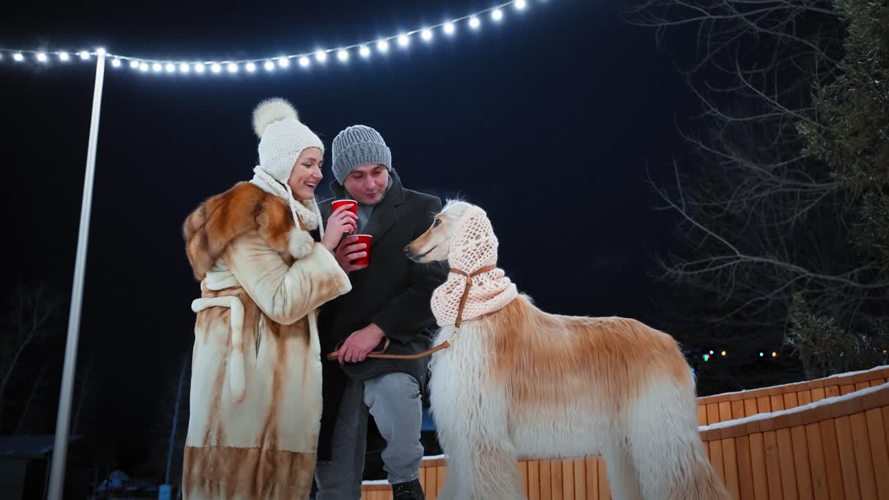 Couple enjoying hot drinks with their dog in the winter night