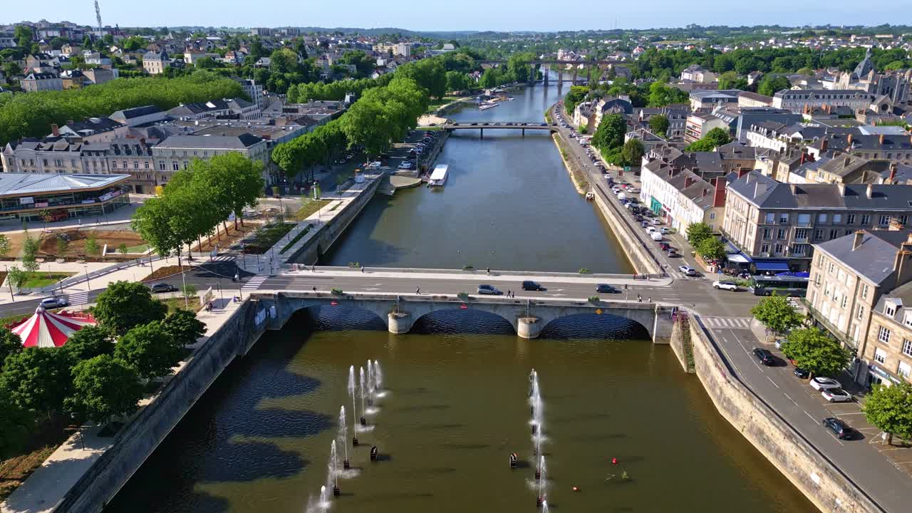 Aerial top-down view over Mayenne shows fountains, the 11 Novembre square, riversides, and a calm bridge under sunligh - France
