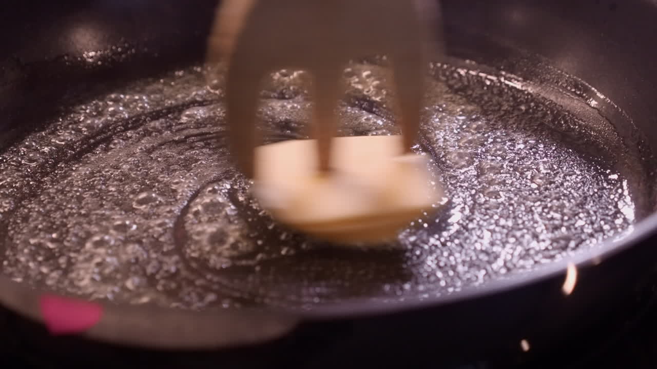Closeup: Butter melts in hot pan on stove, stirred with wooden fork