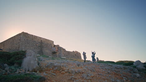 happy couple silhouettes photographing together at sunset cliff. people filming