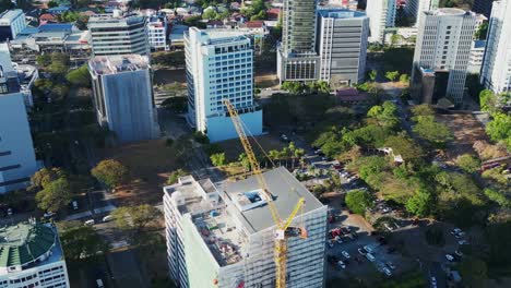 Retroceso-Aéreo-Revela-El-Sitio-De-Construcción-De-Un-Edificio-Moderno-Y-Una-Grúa-Con-Un-Impresionante-Paisaje-Urbano-Asiático-En-Alabang,-Ciudad-De-Muntinlupa,-Filipinas