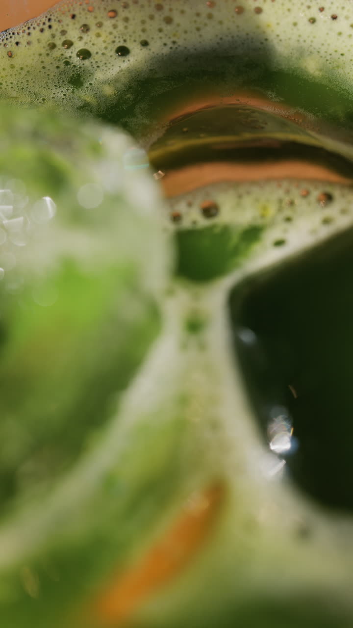 Close up of a glass of an iced orange juice matcha on a table at a cafe. Vertical