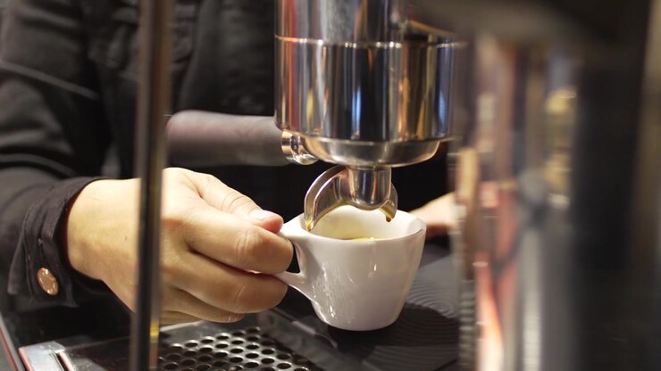 Primo piano di una mano che tiene una tazza di caffè espresso sotto il portafiltro durante l'estrazione attiva in un bar.