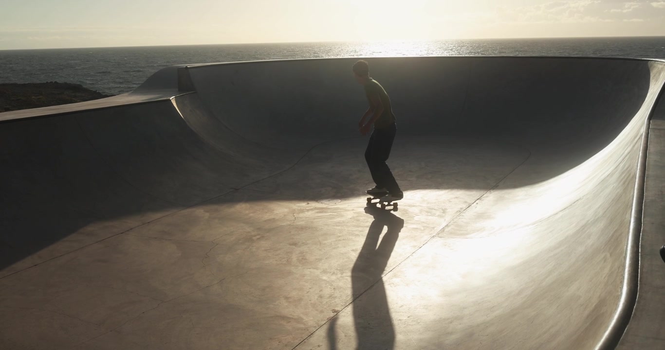 Skateboarder in una bowl di cemento con vista mare al tramonto