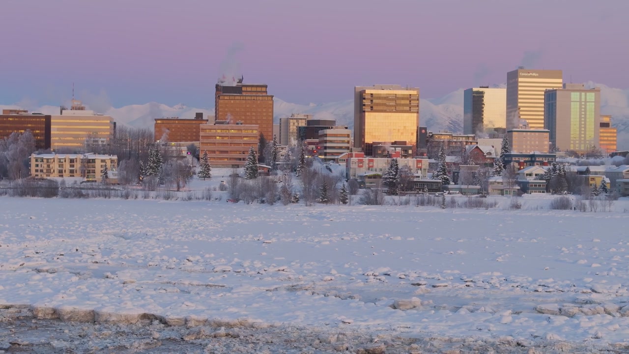 Skyline invernale della città di Anchorage, Alaska, ripresa con drone in movimento di edifici illuminati dalla luce del crepuscolo con ghiaccio in primo piano.