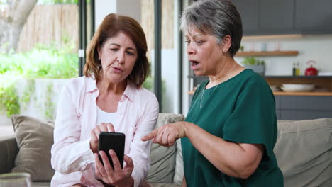 senior women discussing smartphone content at home, sharing opinions and emotions