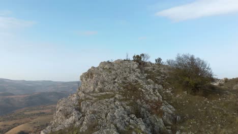 tracking aerial shot over rocky hill, valley and forest as background