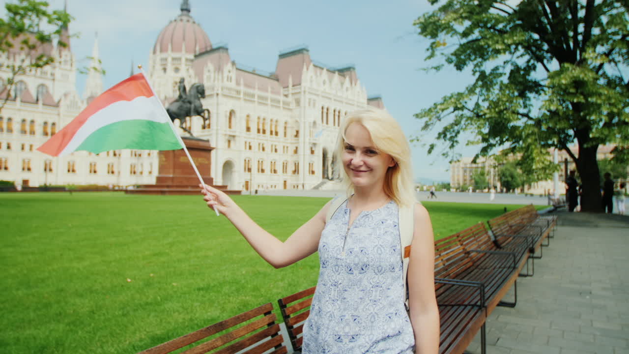 부다페스트에서 의회의 배경에 헝가리 국기와 함께 포즈를 취하는 젊은 여성 관광