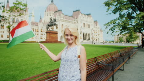 junge touristin, die mit der ungarischen flagge auf dem hintergrund des parlaments in budapest posiert