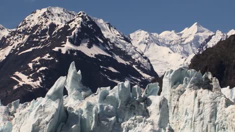 Jagged-peaks-of-ice-on-top-of-Margerie-Glacier,-snow-capped-mountains-in-the-background