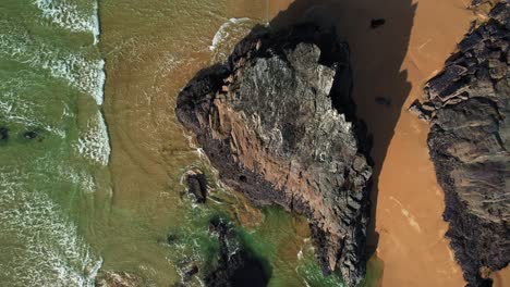 Fotografía-Cenital-De-Formaciones-Rocosas-De-Bedruthan-Steps-Con-Olas-Del-Océano-Rodando-Sobre-Arena-Dorada,-Cornualles