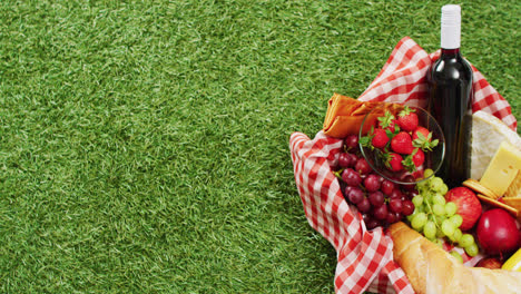 picnic basket with checkered blanket, fruits, bread, cheese and wine on grass with copy space