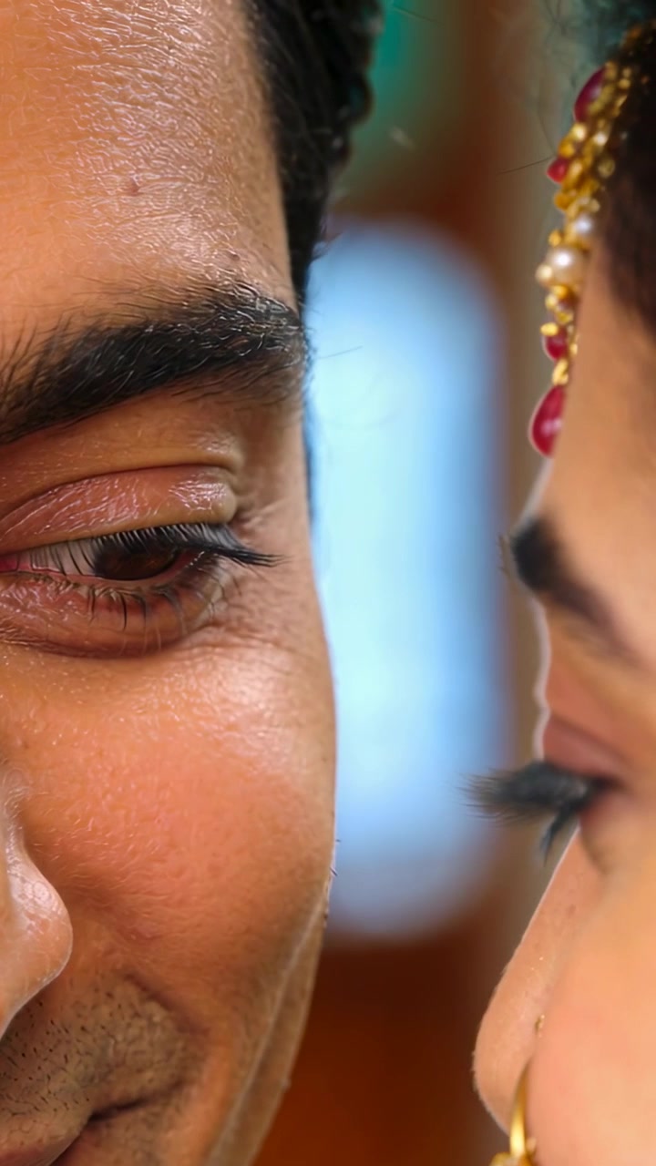 Vertical video: Holding gaze, man and woman leaning closer in room, with nose hoop and maang tikka
