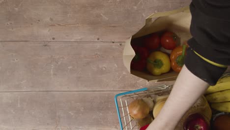 overhead shot of person taking basic fresh food items from paper bag and putting them into supermarket shopping basket