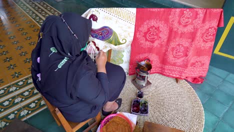 rear view of muslim woman creating unique batik motif on fabric using melted wax