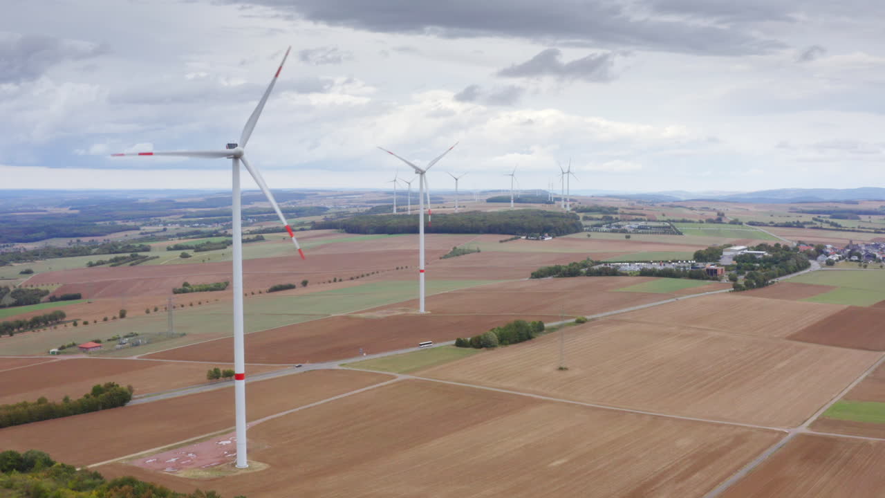High Quality aerial view of wide fields with tall wind turbines above autumn trees calm sky renewable energy landscape in Luxembourg clean light soft colors and a peaceful cinematic atmosphere