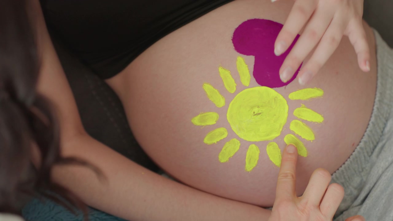 Mani che dipingono un sole e un cuore sulla pancia di una donna incinta