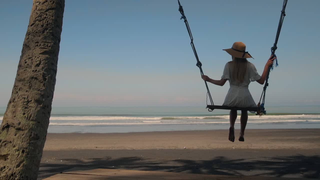 mujer balanceándose en un columpio de playa en la costa tropical