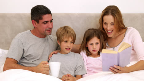 Padres-E-Hijos-Sonrientes-Leyendo-Juntos-En-La-Cama.