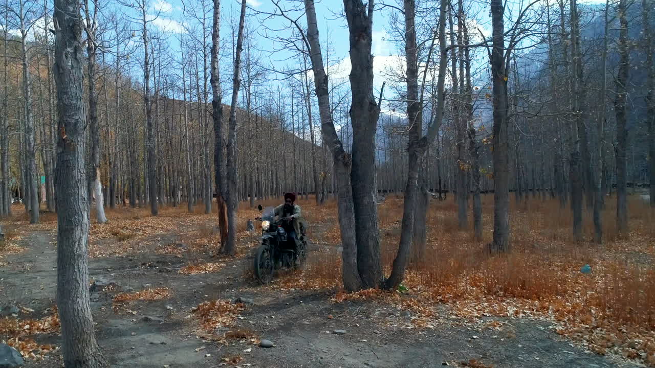 Front view of solo motorbiker cruising and exploring high altitude forest area during autumn under Himalayas