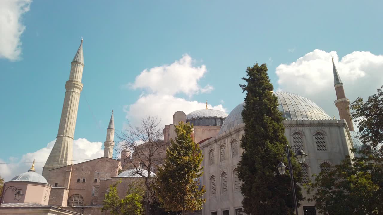 durante el día, bajo cielos parcialmente nublados, cámara lenta cinematográfica, mezquita de hagia sophia con sus minaretes y algunos árboles en primer plano