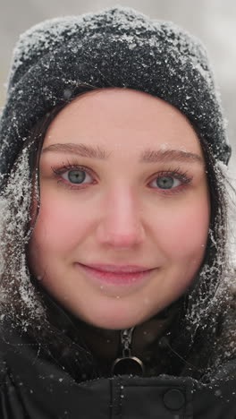 joven de pie en un entorno invernal sereno con chaqueta negra y gorra, copos de nieve descansando suavemente en su cabello, figura borrosa caminando en el fondo