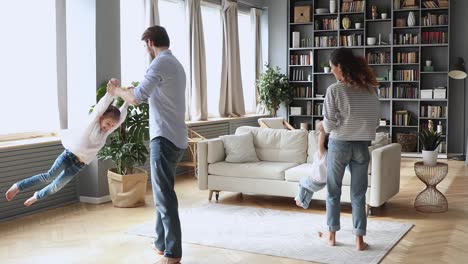 happy parents dancing with funny small kids sisters at home.