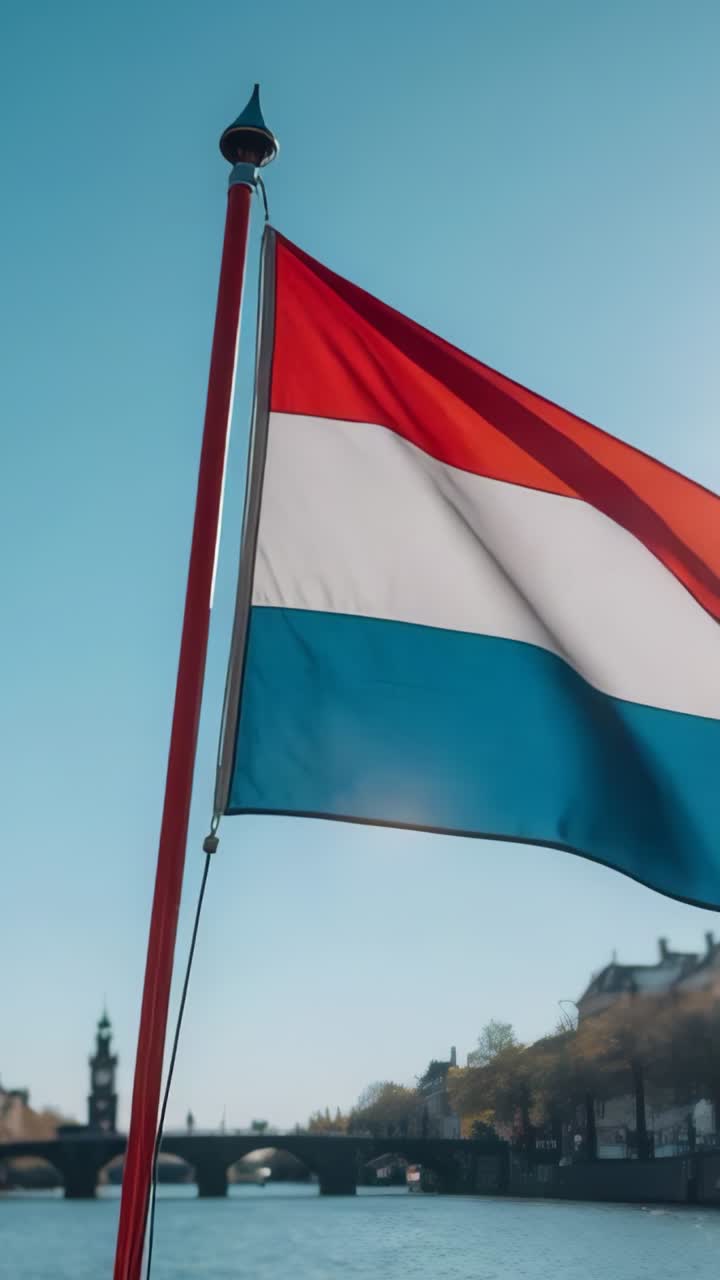 Vertical video: Waving Luxembourg tricolor flag in breeze on pole by river, stone bridge