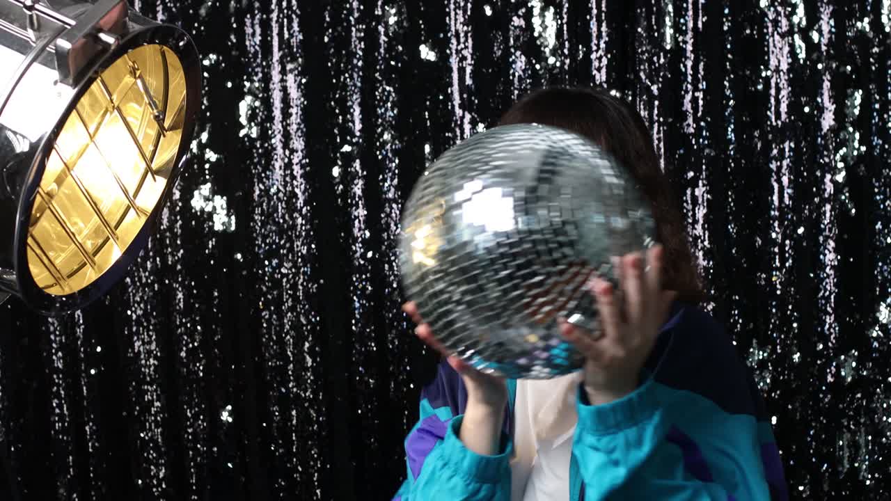 joven mujer deportiva estilo de los años 80 y 90. chica positiva de la moda de los años 90 en una fiesta de discoteca con una pelota de discotecas en las manos