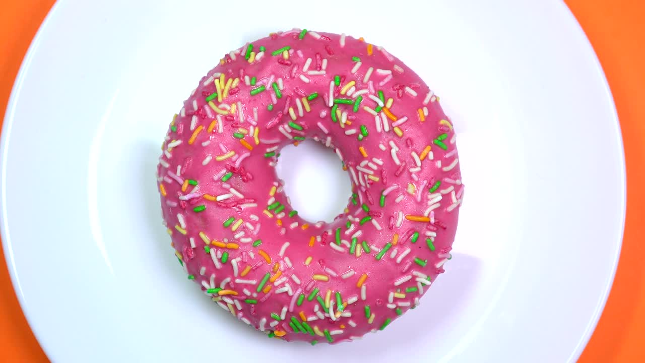 brillantes y coloridas salpicaduras de rosquilla, tiro macro, girando rápidamente en un plato sobre un fondo naranja.