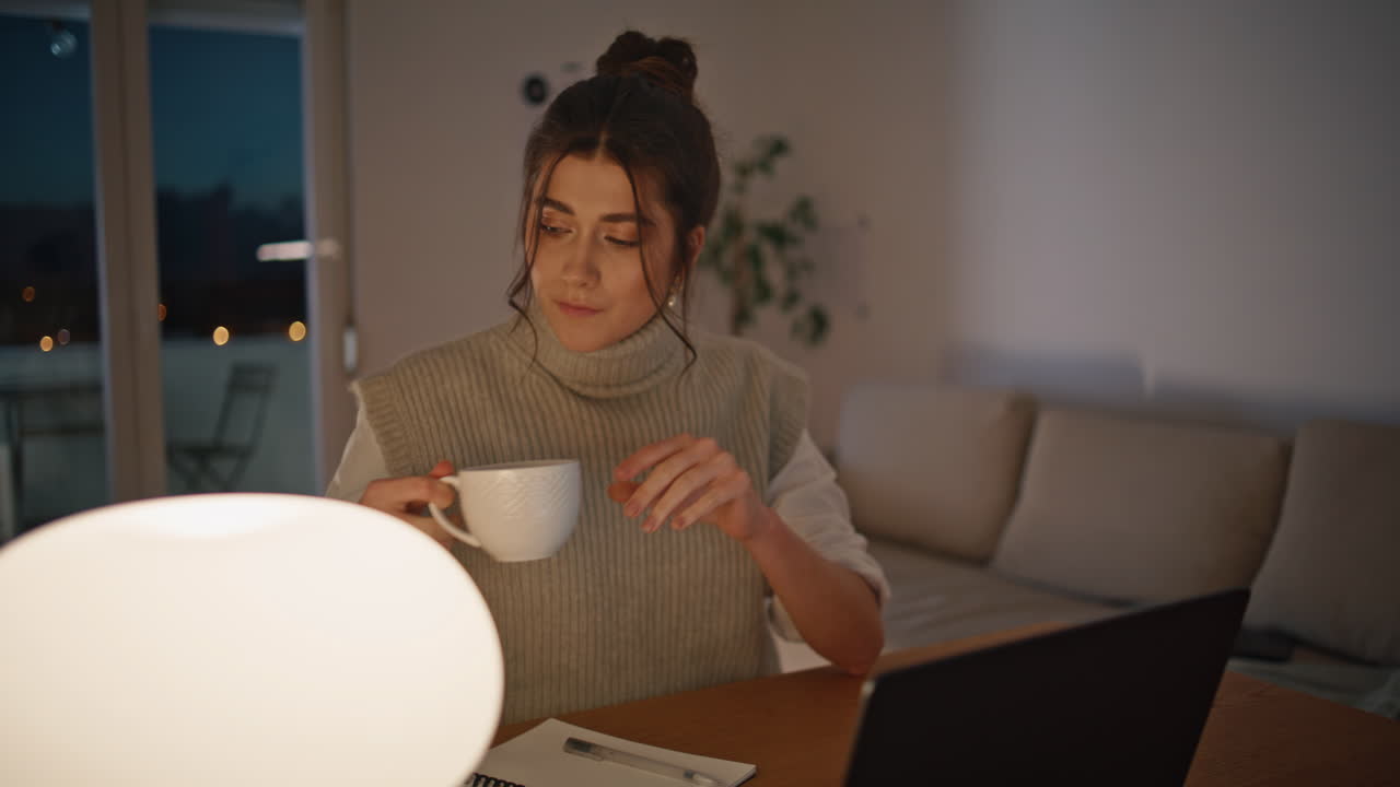 freelance de la noche bebiendo café mirando portátil en el hogar en el lugar de trabajo de cerca