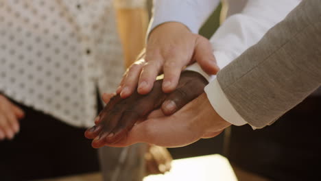 Multiethnic-business-team-hands-putting-on-each-others-as-a-team-on-white-wooden-table