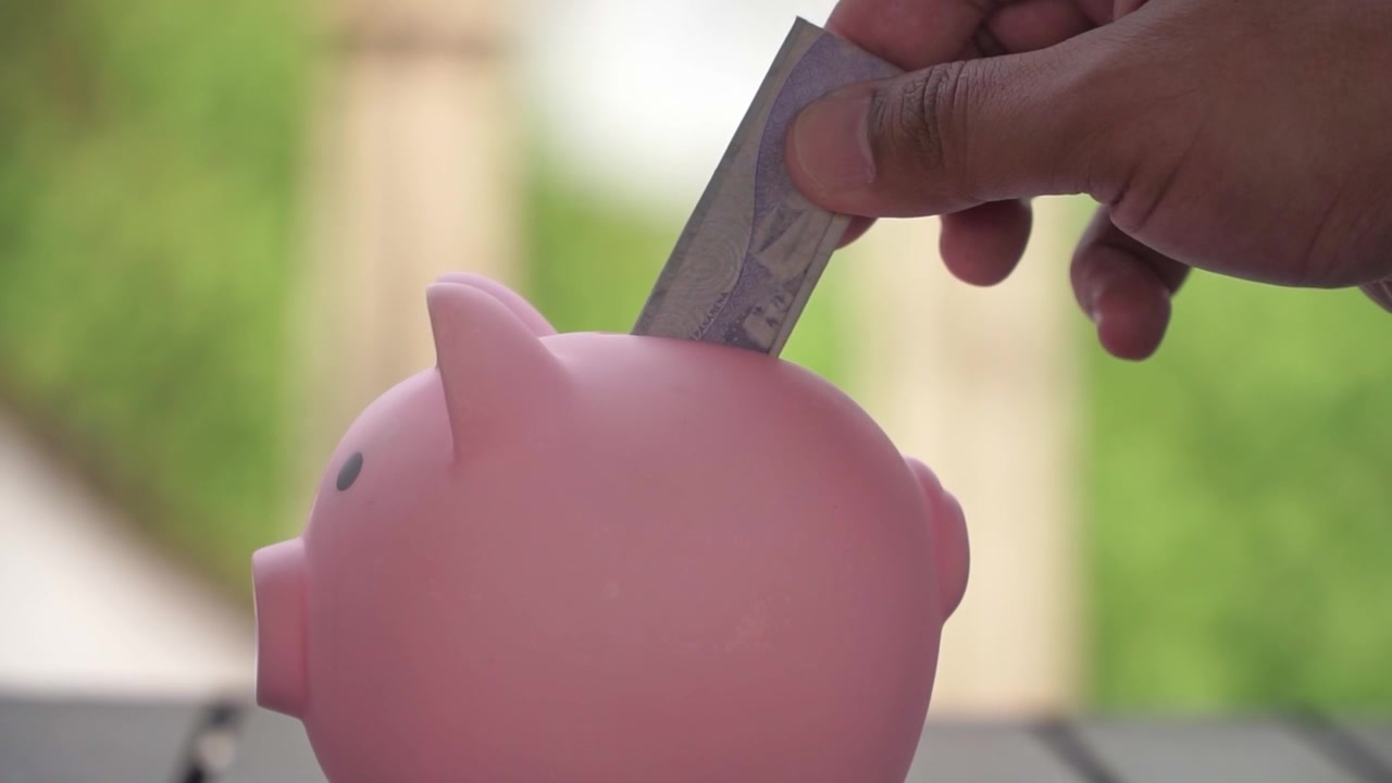 Close-up hand inserting coin into piggy bank, financial success and budgeting illustration. Personal finance concept with piggy bank and coins.