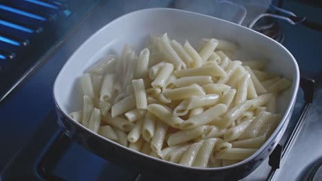Poring-steaming-cooked-pasta-into-porcelain-bowl