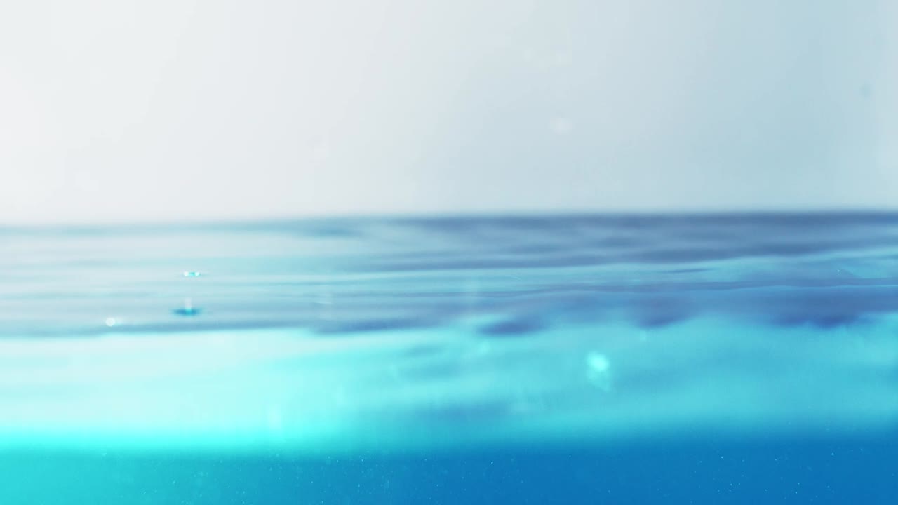 슬로우 모션의 깨끗한 물 표면은 물이 튀는 상점으로 화면을 채우고 기포로 액체 표면을 흔들고 있습니다.