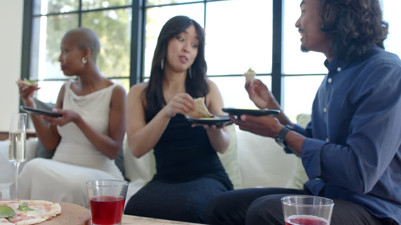 African American friends spotting pizzas, reaching, passing and eating slices on sofa sharing meal