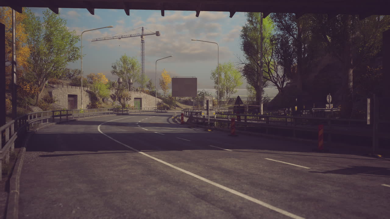 Empty road under a bridge with trees and distant construction activity