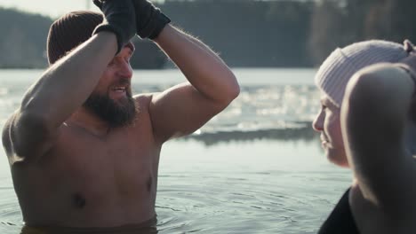 hombre y mujer caucásicos charlando mientras están de pie en el lago congelado en invierno con las manos en alto.